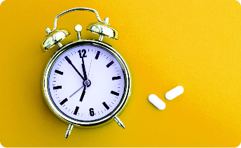 Alarm clock next to two white pills on a yellow background.